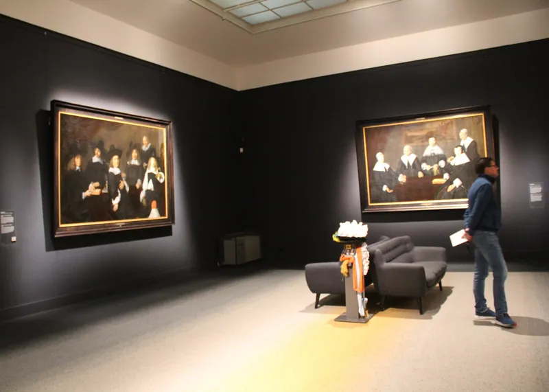Een bezoeker loopt door een donkere museumzaal met twee groepsportretten van Frans Hals.